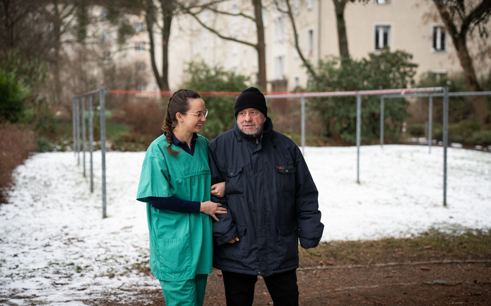 Pflegekraft begleitet einen älteren Mann bei einem Spaziergang im Park