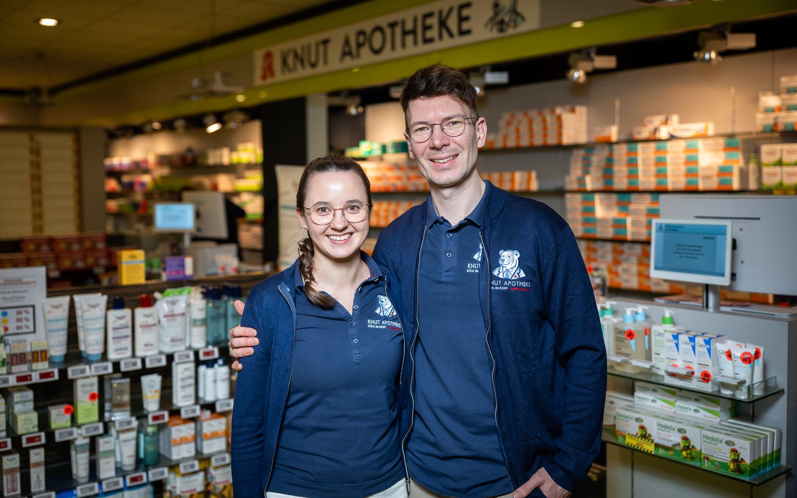 Apotheker und PTA stehen lächelnd im Verkaufsraum der Knut-Apotheke