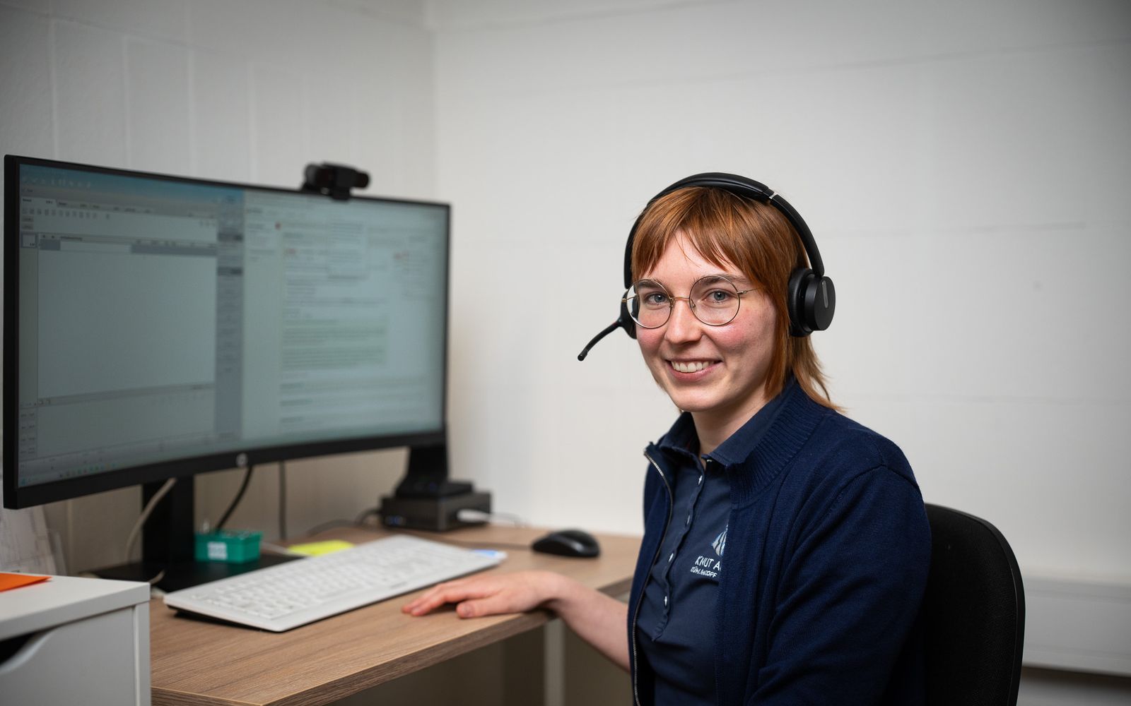 Mitarbeiterin mit Headset am Schreibtisch vor dem Monitor