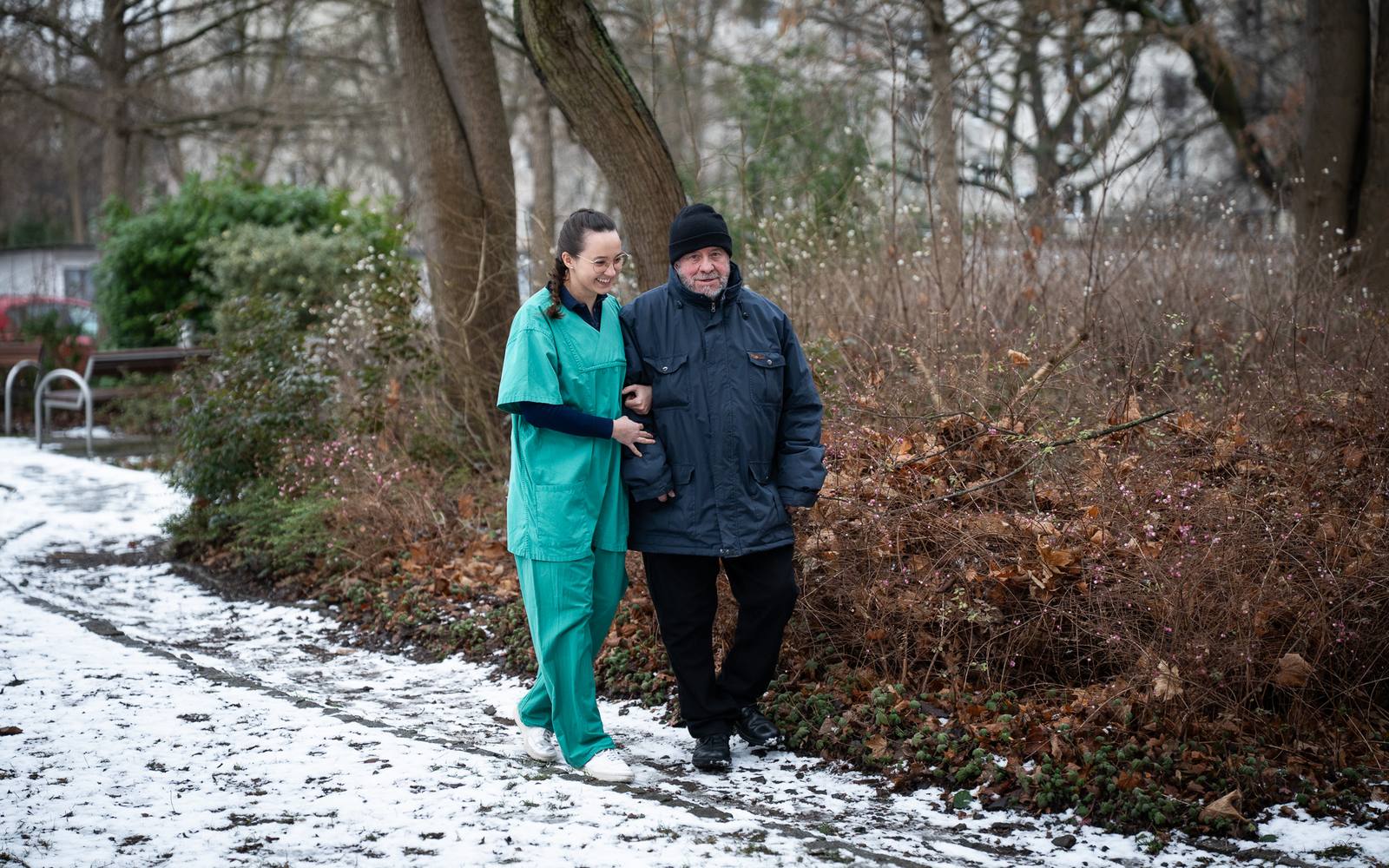 Pflegekraft geht mit einem älteren Mann durch einen verschneiten Park