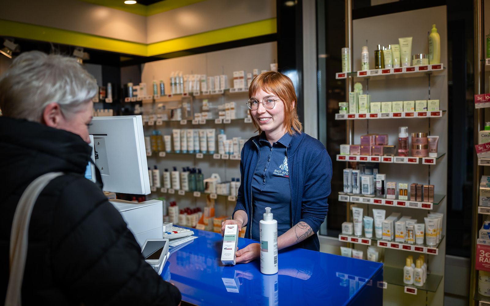 Mitarbeiterin der Knut-Apotheke berät eine Kundin am Handverkaufstisch